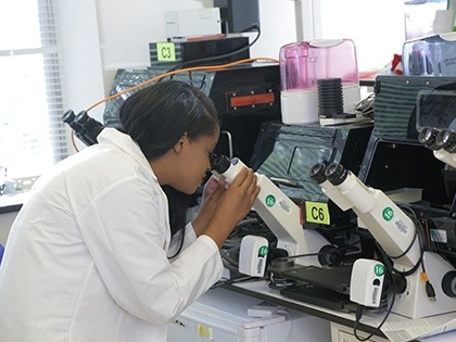woman in white coat looking in microscope