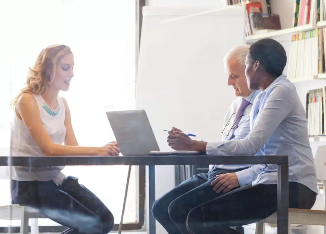 several people sitting across a desk from each other, discussing work.