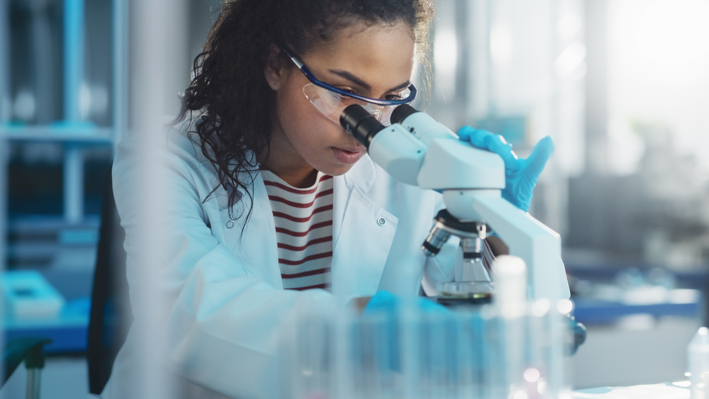 Portrait of Beautiful Black Scientist Looking Under Microscope Does Analysis of Test Sample.