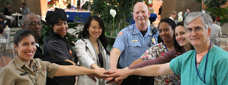 eight NIH Clinical Center staff in a circle with their hands stacked together 
