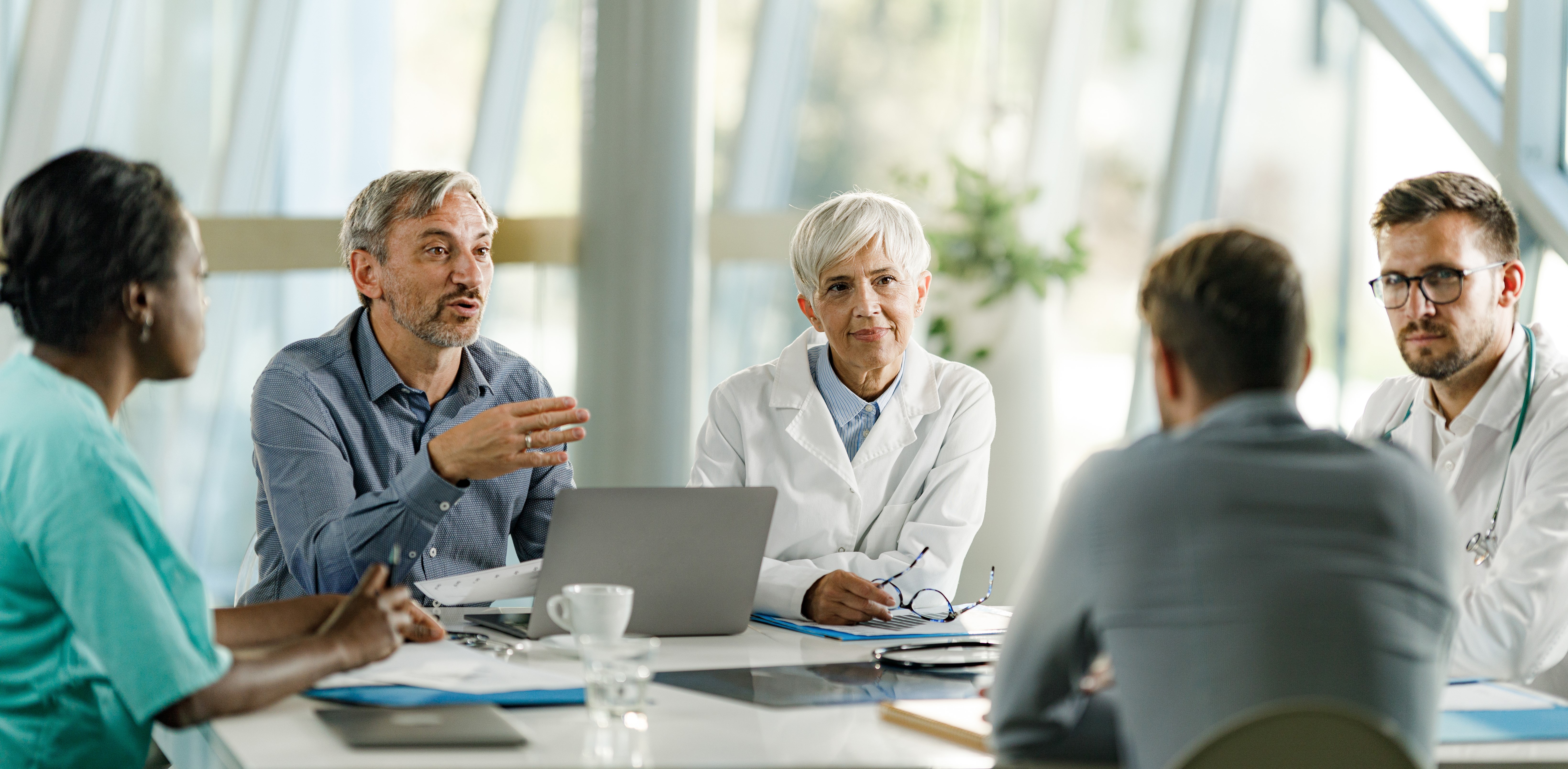 Five healthcare professionals gather at a conference table in discussion.