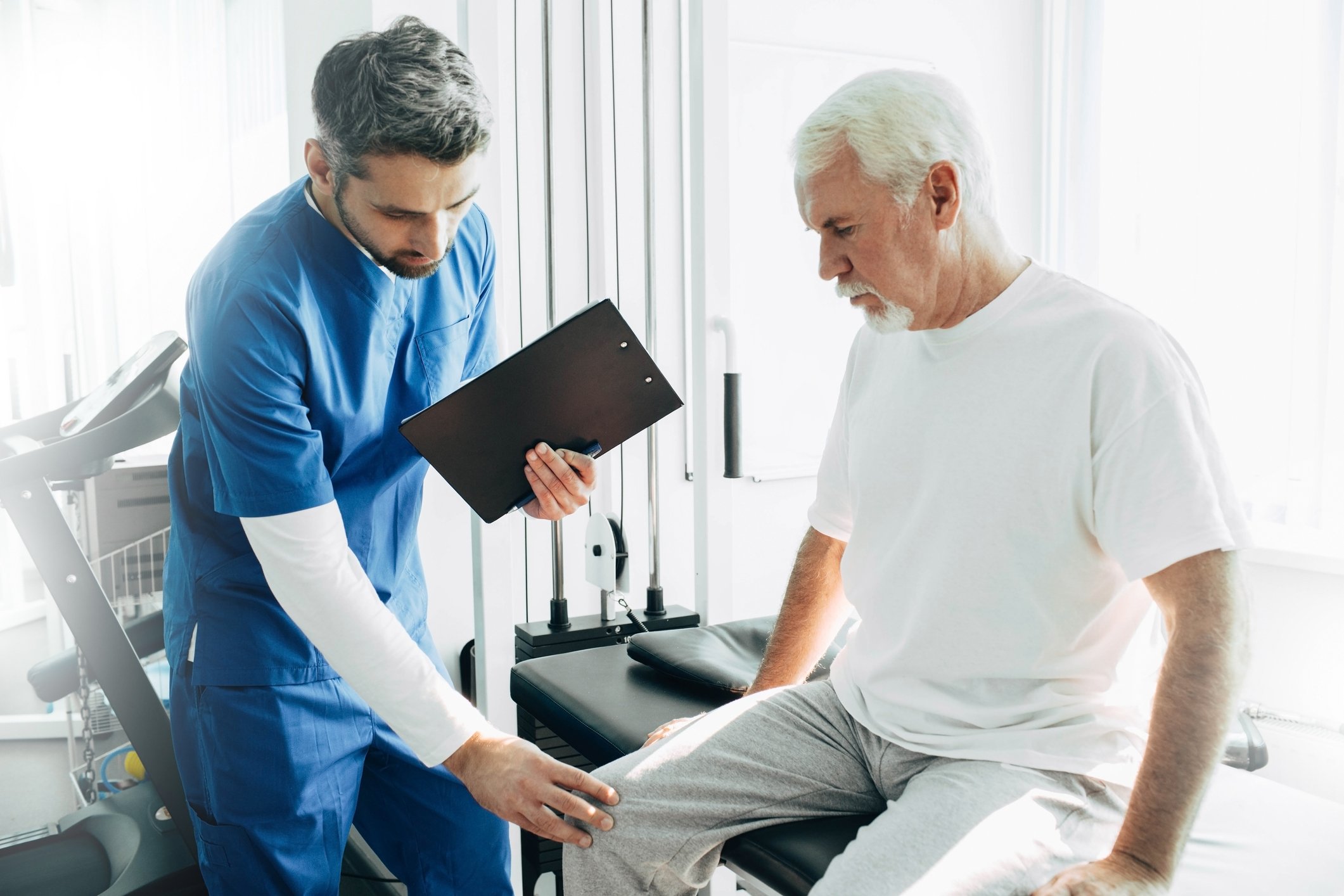 Health professional examining senior man's knee.