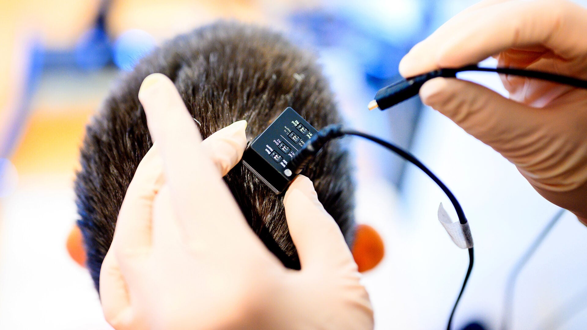 Researcher plugging a cable into a device on a person’s head.