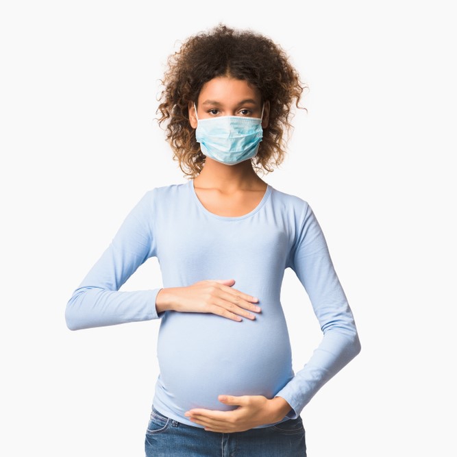 Black woman wearing a mask and holding her belly.