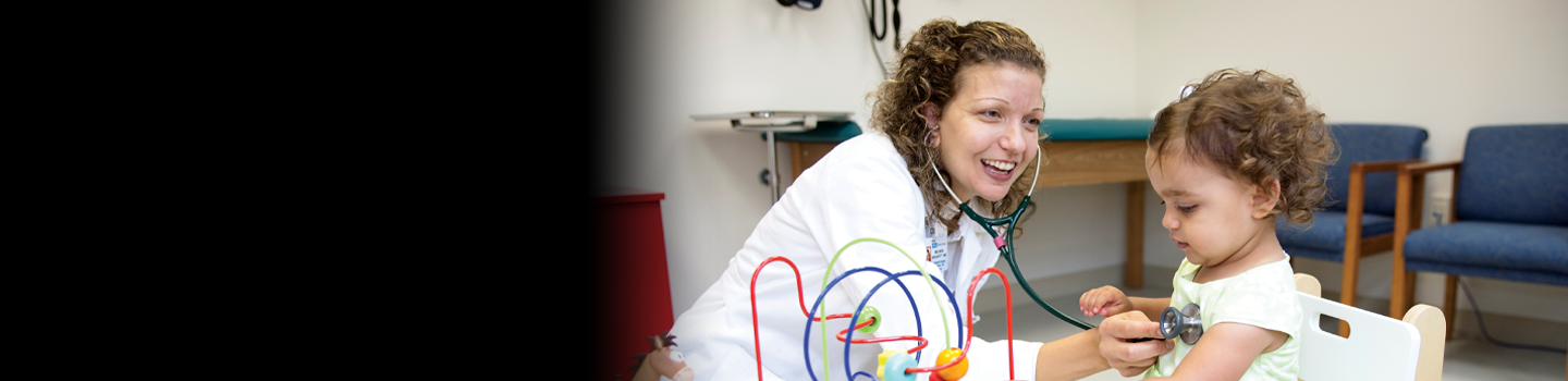 Pediatrician listening to a child's heart with a stethoscope while sitting at a table with toys.