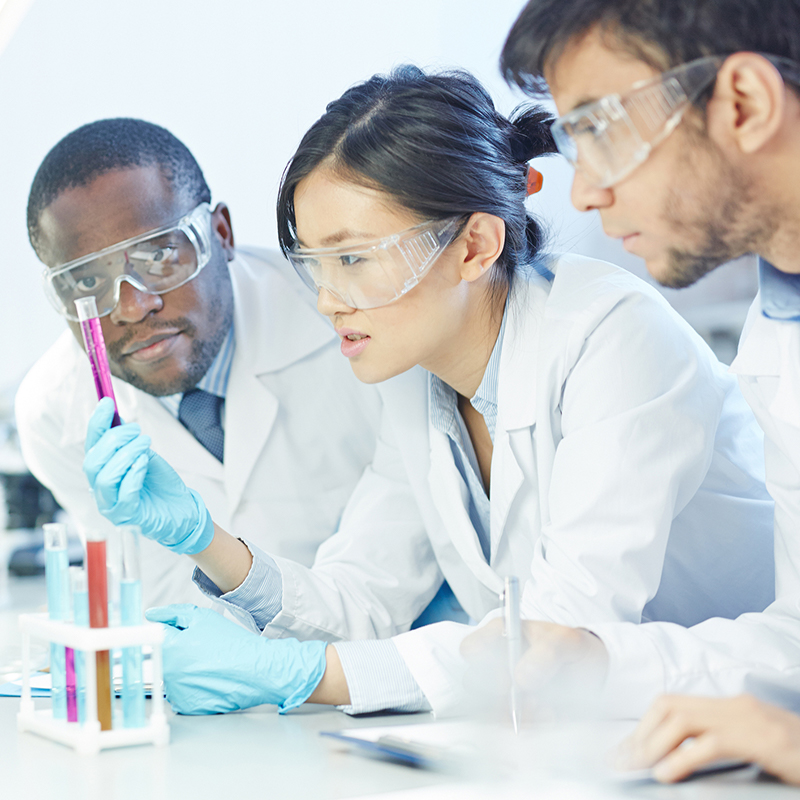 Three scientists wearing goggles looking at a test tube