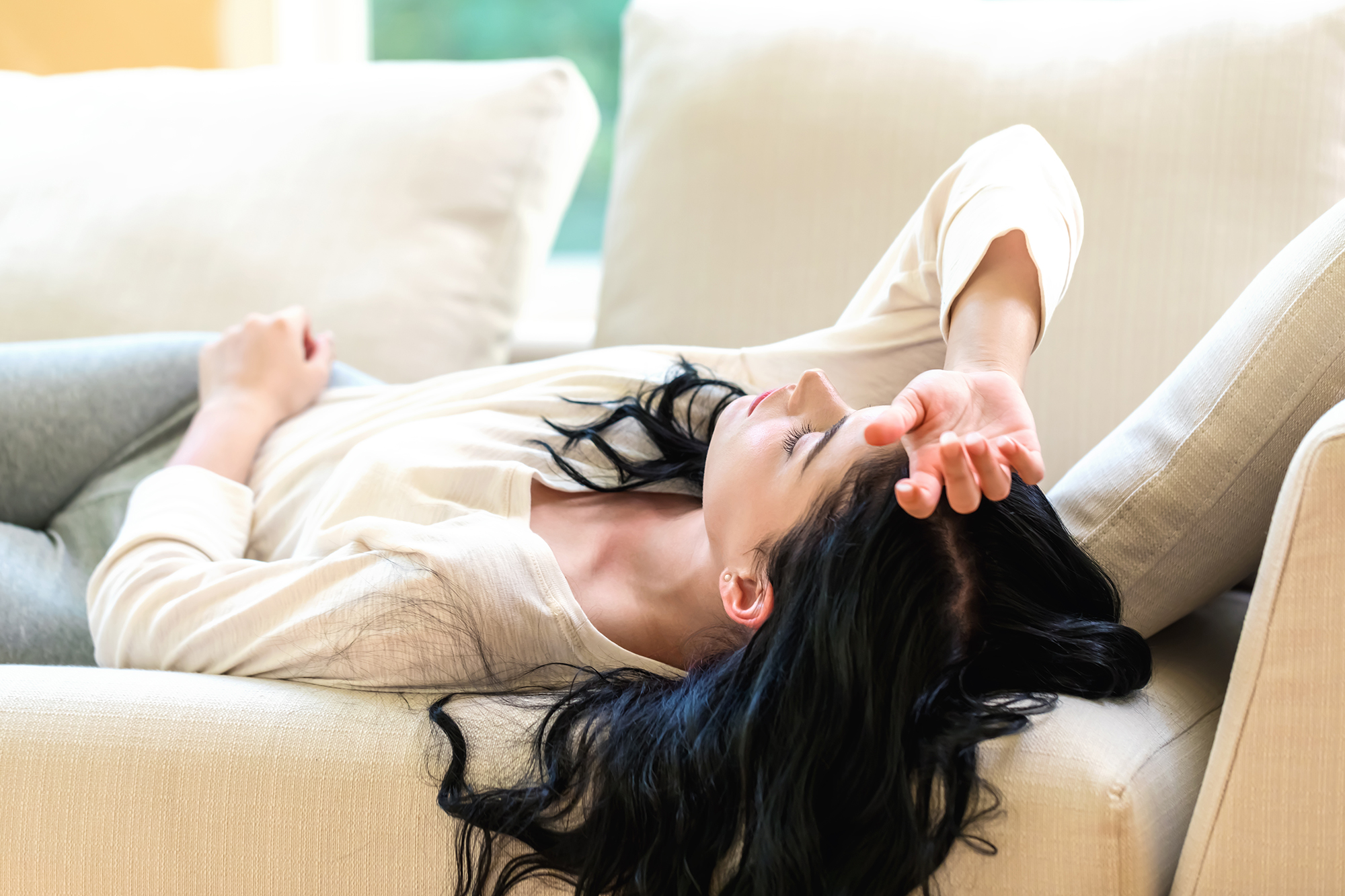 Young woman lying on a sofa with her eyes shut.