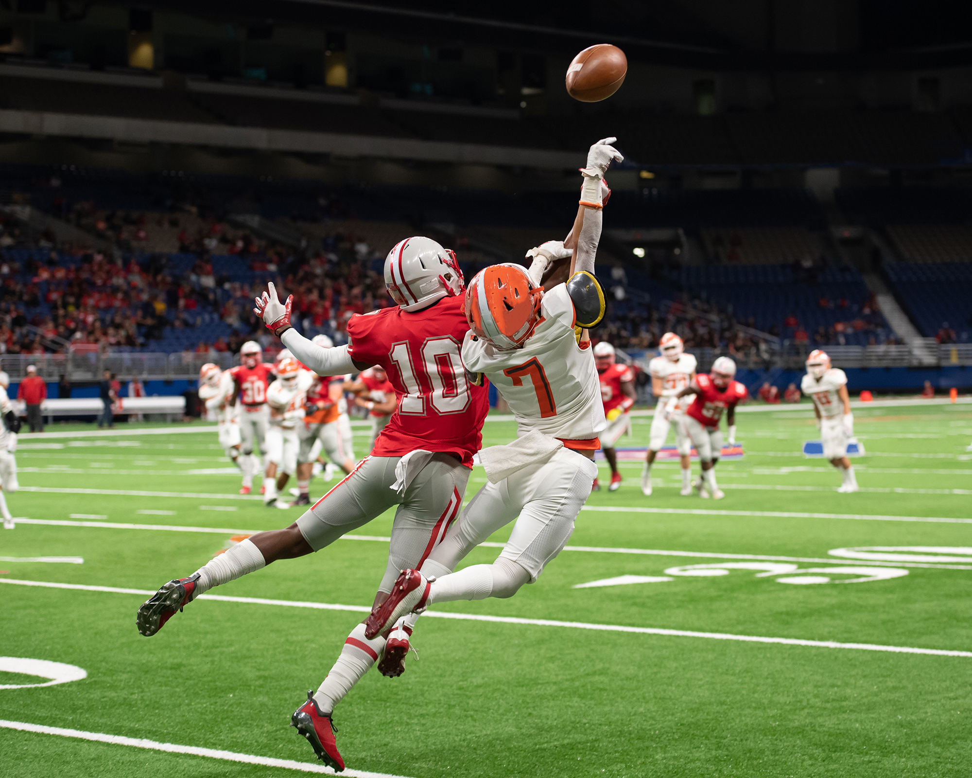 Football players on the field leap to catch the ball.