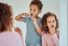 Children are looking in the mirror at their teeth.