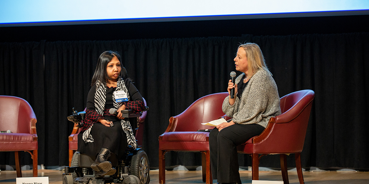 Two people sitting in chairs holding a microphone in front of a screen.