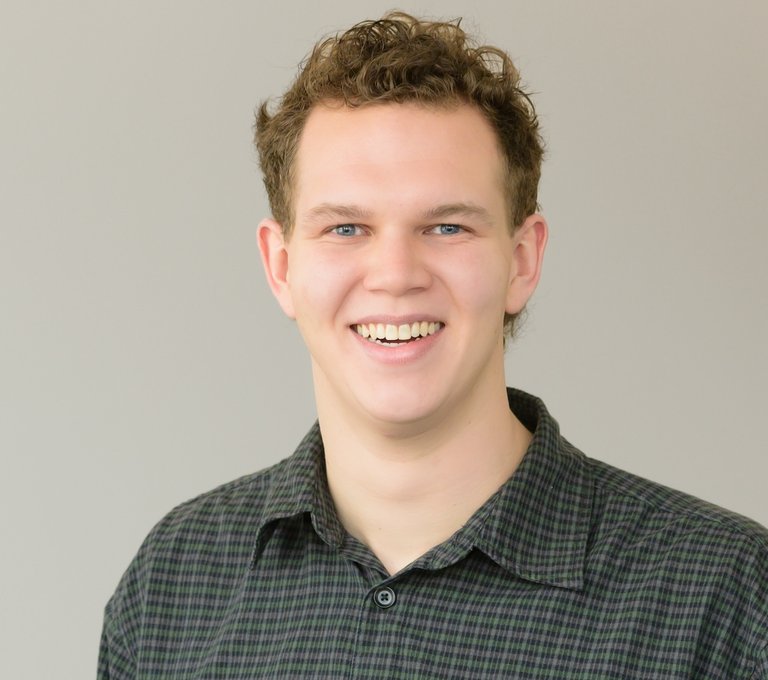 A headshot of a smiling man in a checkered green shirt