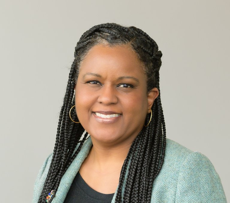 A women with long braids and a light turquoise blazer, smiling at the camera