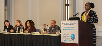 During the CUGH 2019 annual meeting woman speaks at podium next a table of four panelists.