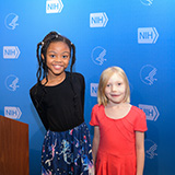 Two children are standing side by side and smiling at the camera.
