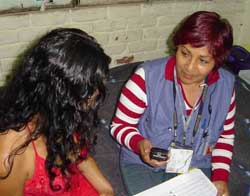 PHOTO: Two women sit on a sofa together, one faces the camera, holding a handheld device, the other’s hair covers her face.