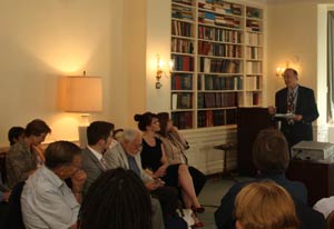 Dr Roger Glass speaks from a podium to an audience full of attentive listeners in the stone house conference room