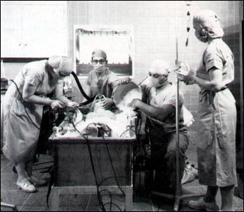 Black and white photo of four people in scrubs and masks in a surgical suite