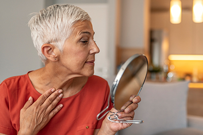 Elderly woman check the appearance of her nick wrinkles in a handheld mirror. 