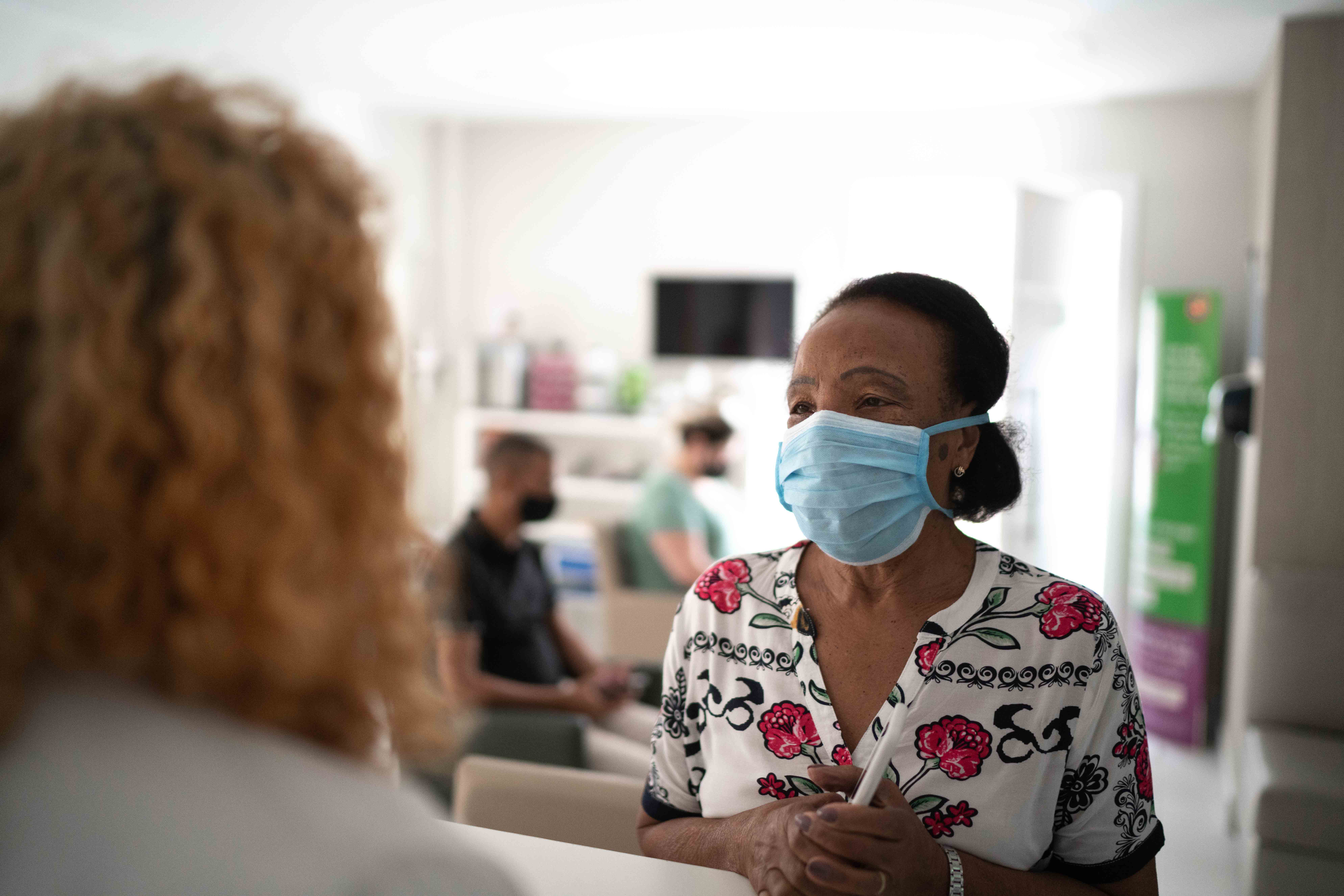 Woman wearing a mask, talking to what appears to be a medical professional