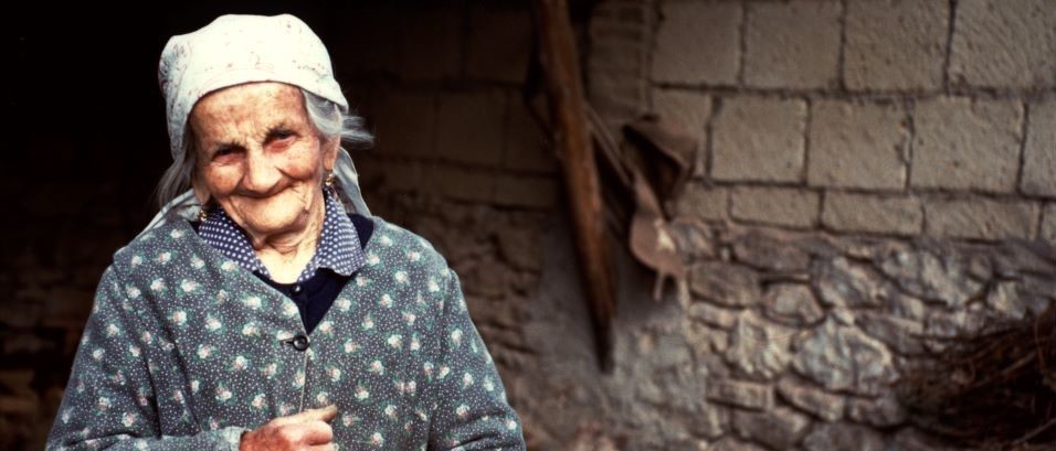 smiling older woman in a coat with flowers on a blue background