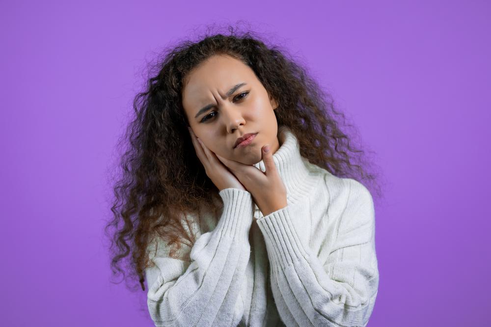 Mujer de cabello rizo se pone la mano en la mejilla en señal de que tiene dolor. 
