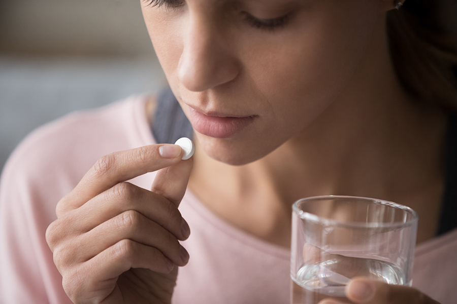 Woman holding pill and glass of water.