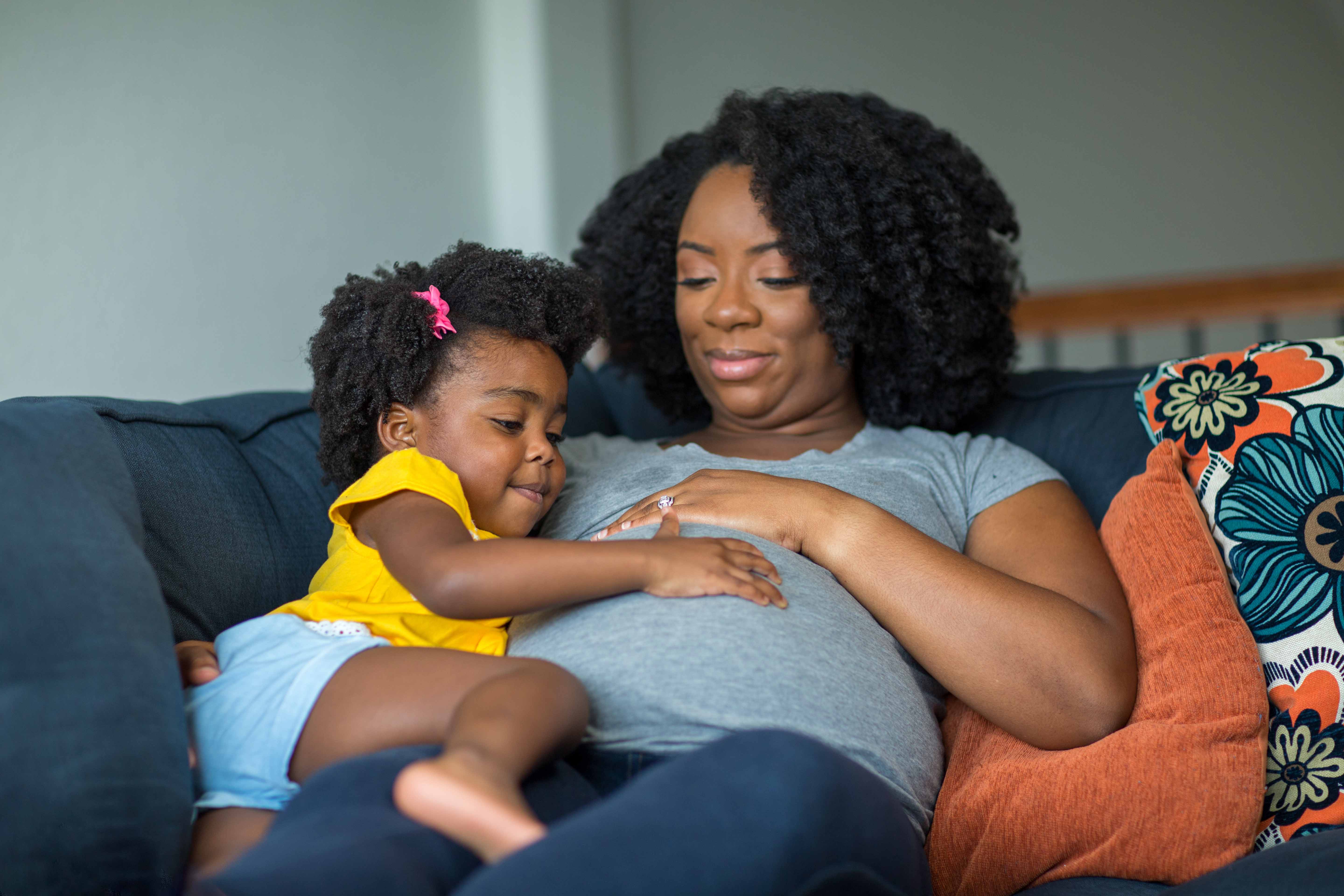 Pregnant black woman holding a child, both looking at belly