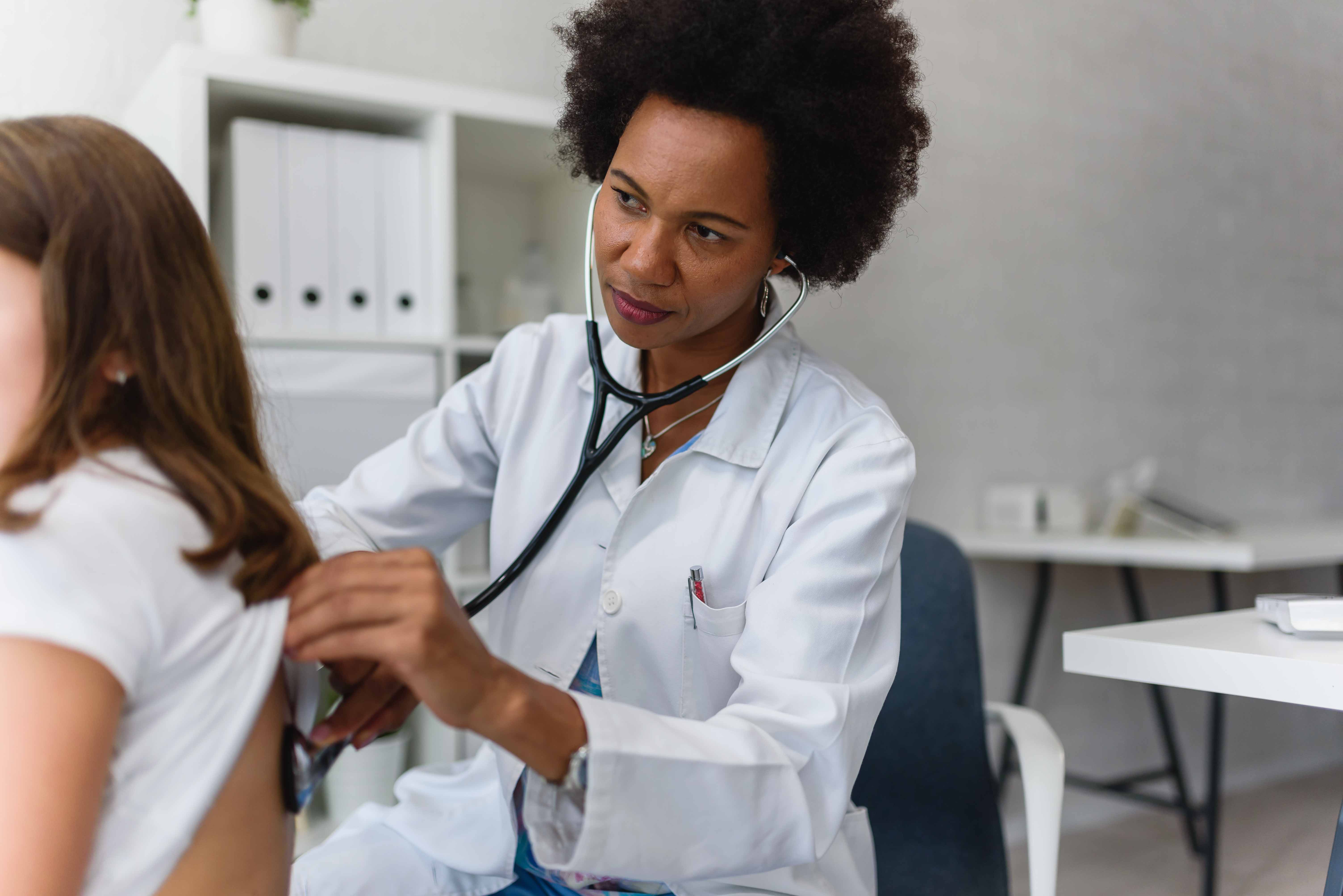 Black female medical professional listening to a patient's lungs through a stethoscope