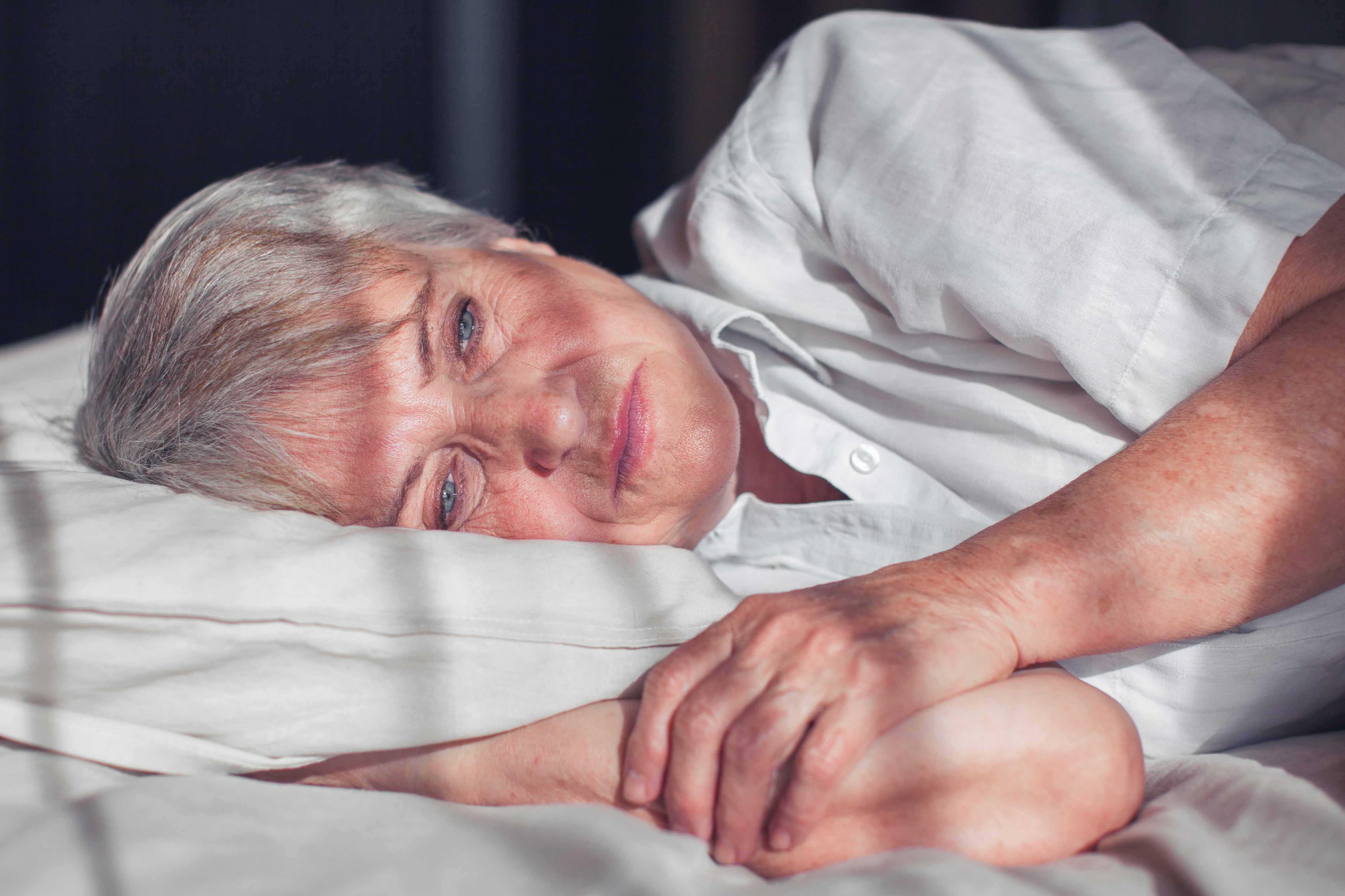 Elderly white woman lying on a bed, awake