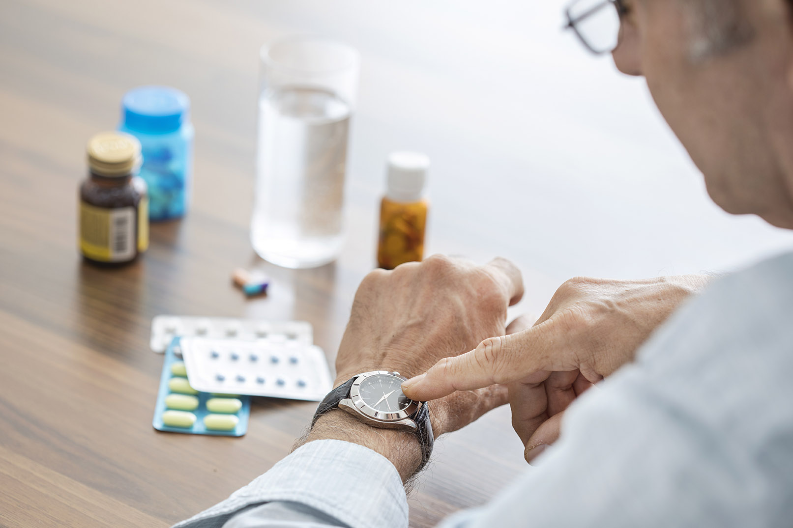 elderly man looking at his watch in front of pills and medicine bottles
