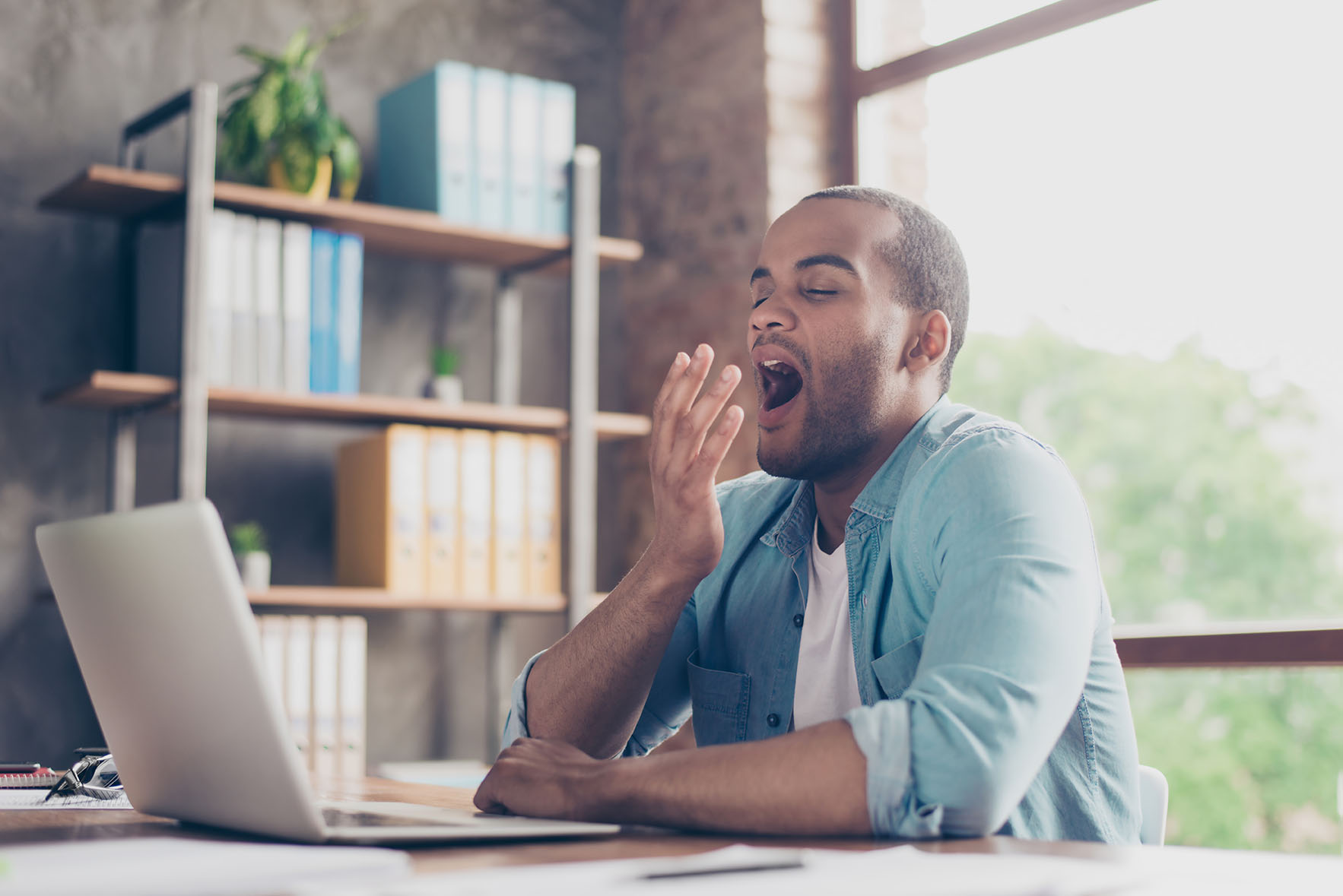 Decorative, african american male looking sleepy, yawning in front of laptop