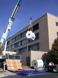 An MRI machine being hoisted into a building by a crane.