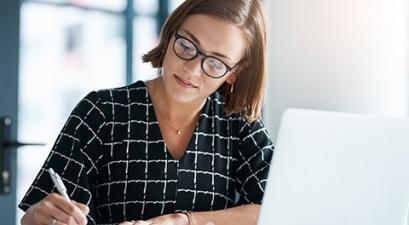 woman sitting by laptop writing on paper