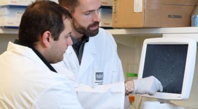 two men in white lab coats looking at screen