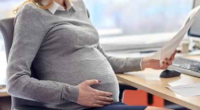 a pregnant woman sitting at a desk reading a document