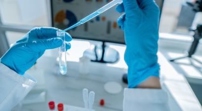 Close up of hands in protective gloves performing a laboratory experiment with a pipette and test tube. Advanced technology and scientific research tools are present on the workbench