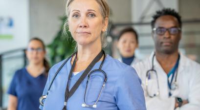 A confident female healthcare professional in scrubs with a stethoscope, standing with three other medical professionals in the background.