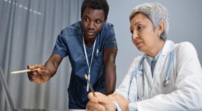 Two healthcare professionals, one in scrubs and the other in a white coat, discussing information on a laptop.