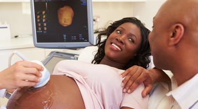 Pregnant woman getting an ultrasound while smiling at a man who has his hand on her shoulder.