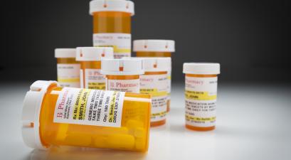 Variety of Non-Proprietary Medicine Bottles on Reflective Surface and Grey Background.