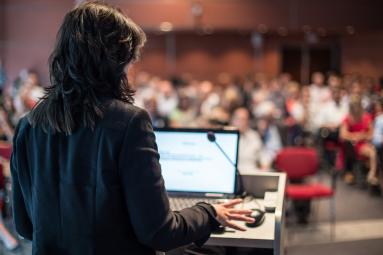 Woman at podium speaking to large audience